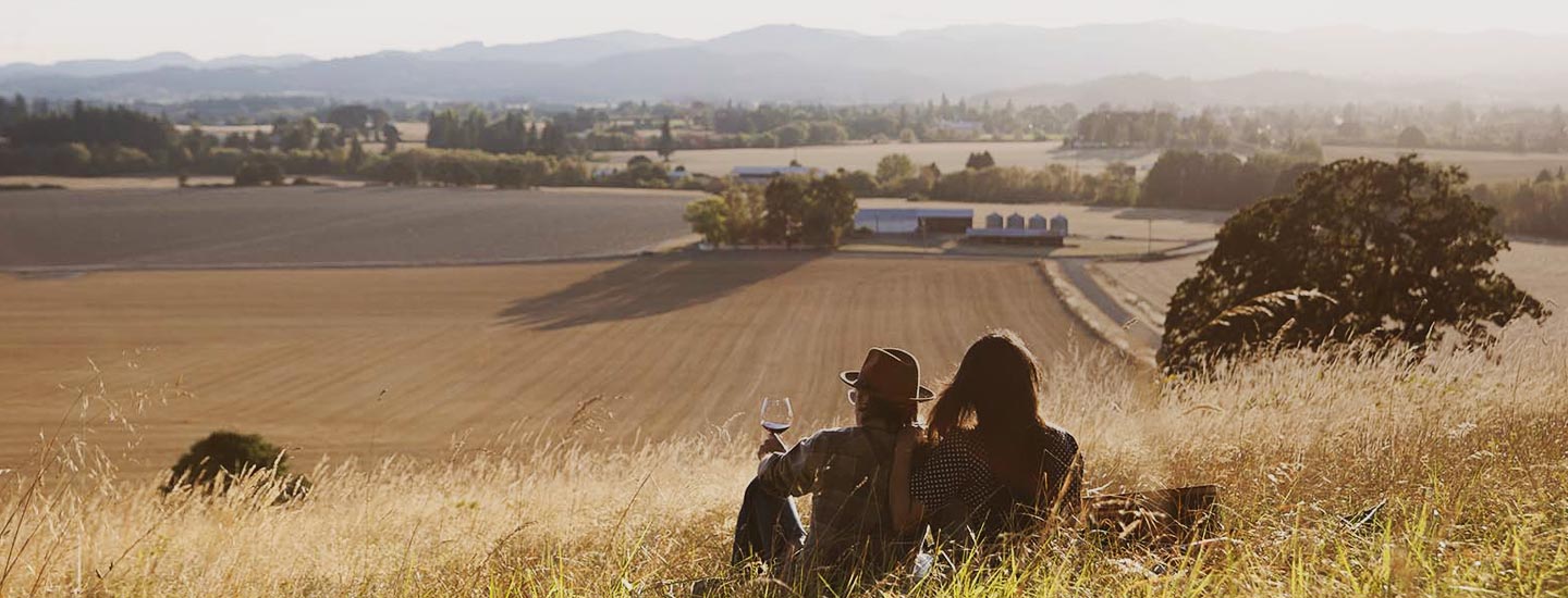 Two people sitting on a hill overlooking a field