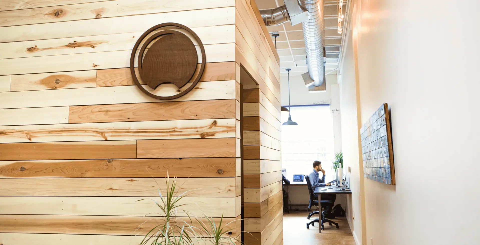 Daylight's Portland office entrance, with a wood-plank wall, the round Daylight logo sign and a team member working at a desk down the hallway